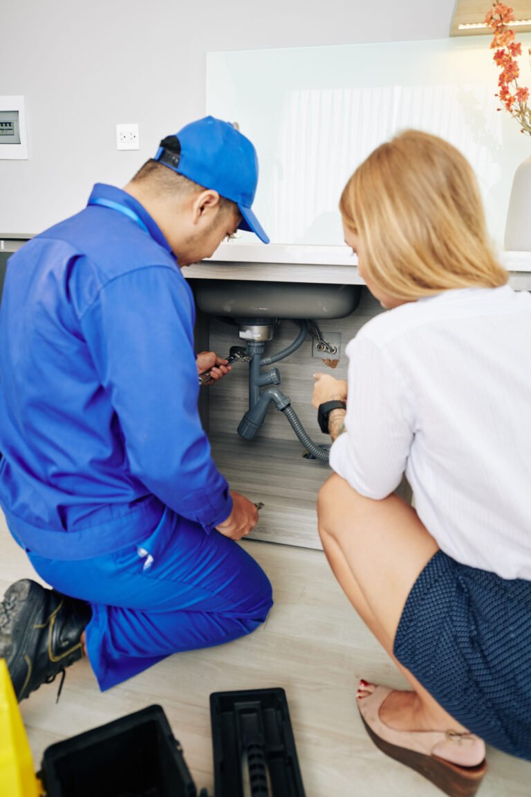 Young woman showing repairman leaky drain under kitchen sink